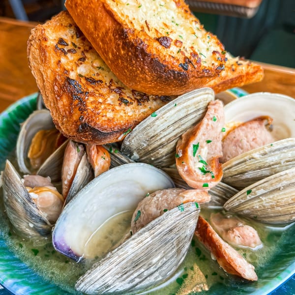Steamed clams in a green bowl with broth and two pieces of toasted garlic bread on top.