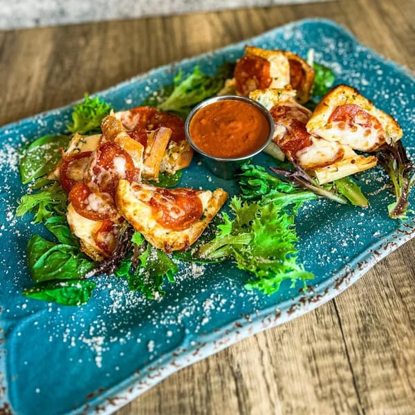 Pepperoni pizza bites with melted cheese and a side of marinara sauce on a blue platter.