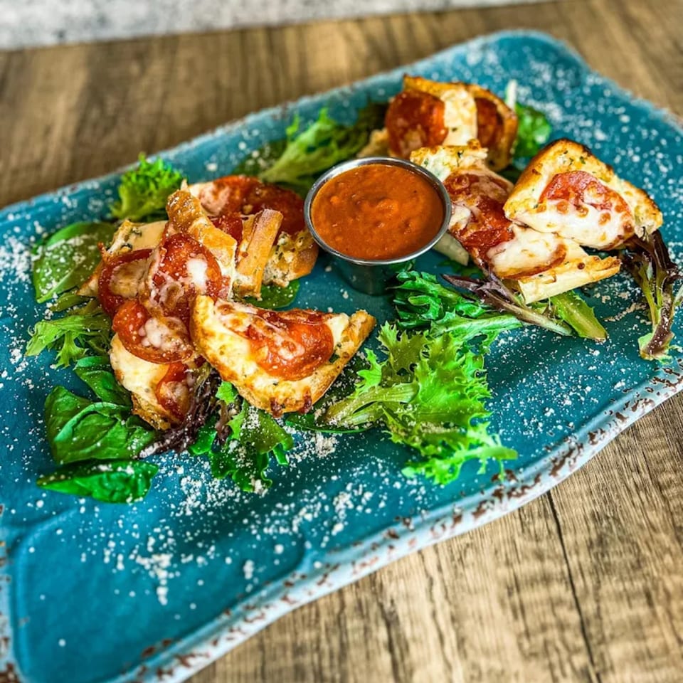Pepperoni pizza bites with melted cheese and a side of marinara sauce on a blue platter.
