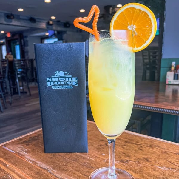 A mimosa with an orange slice and heart-shaped straw next to a Shore House Tavern menu.
