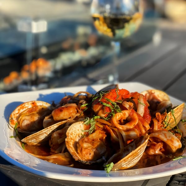 Seafood pasta with clams, calamari, and red sauce, garnished with basil, next to a glass of white wine.