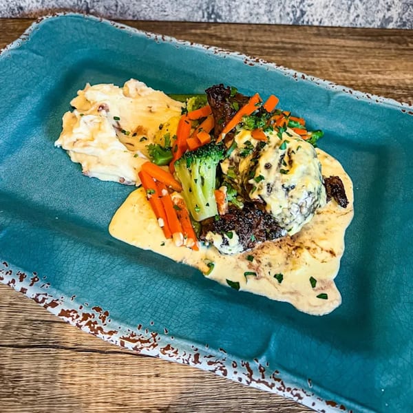 Shore House Tavern's steak with mashed potatoes, broccoli, carrots, and creamy sauce on a teal plate.
