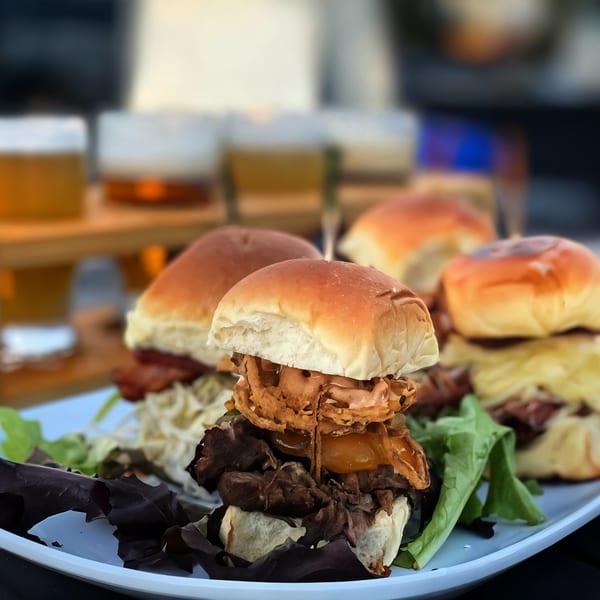 A plate of Shore House Tavern sliders with beef, cheese, and crispy onions, alongside beer flights.