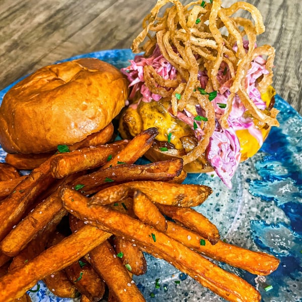 Shore House Tavern's burger with crispy onions, coleslaw, and sweet potato fries on a blue plate.