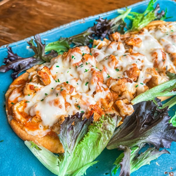 Cheesy chicken flatbread with green and red lettuce on a blue plate at The Shore House Tavern.