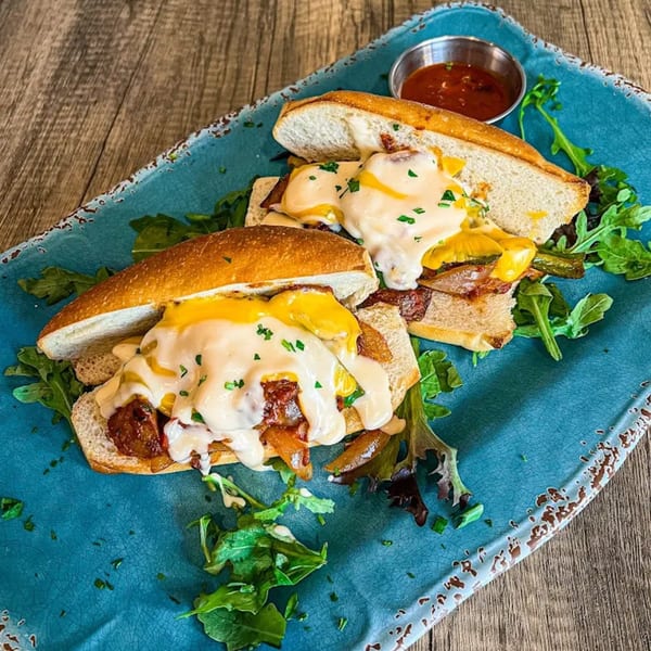 Two open-faced sandwiches with melted cheese, sauce, and greens on a blue plate with a side of red sauce.